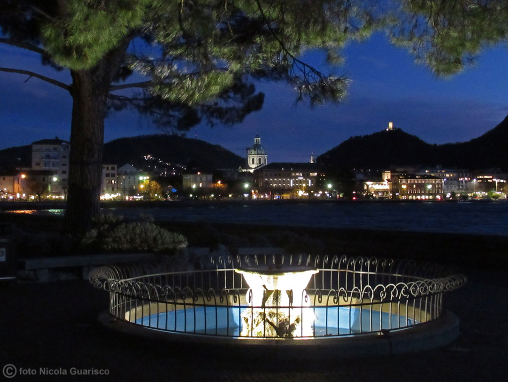 la fontana dei giardini ramelli sul lungolago nei pressi di viale geno sul lago di como con la vista sulla città di notte illuminata