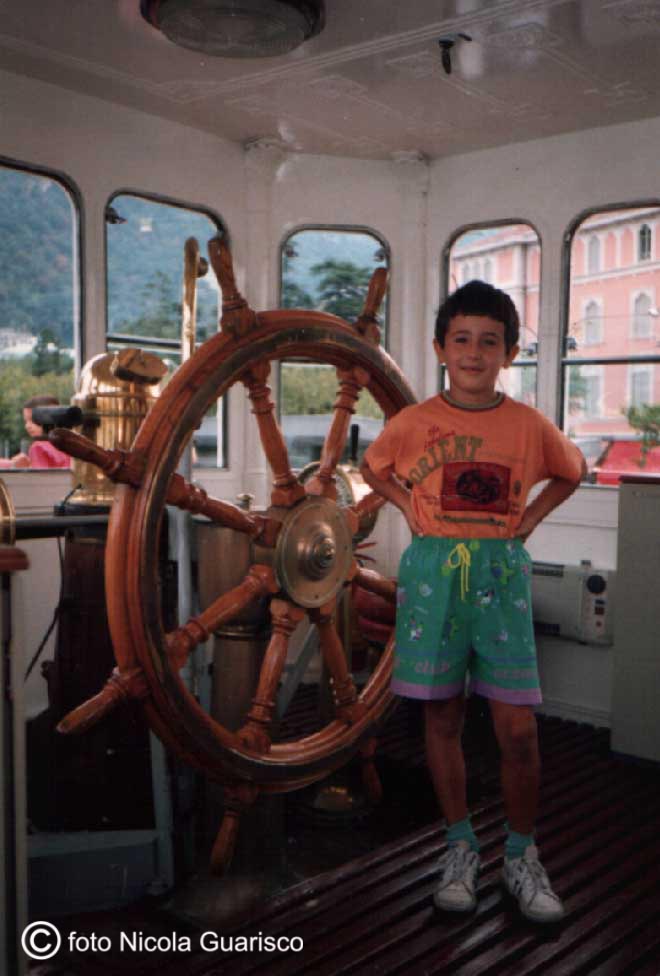 bambino a fianco del timone o timoneria a ruota nella cabina di comando del piroscafo concordia lago di como in navigazione, battello nave a vapore